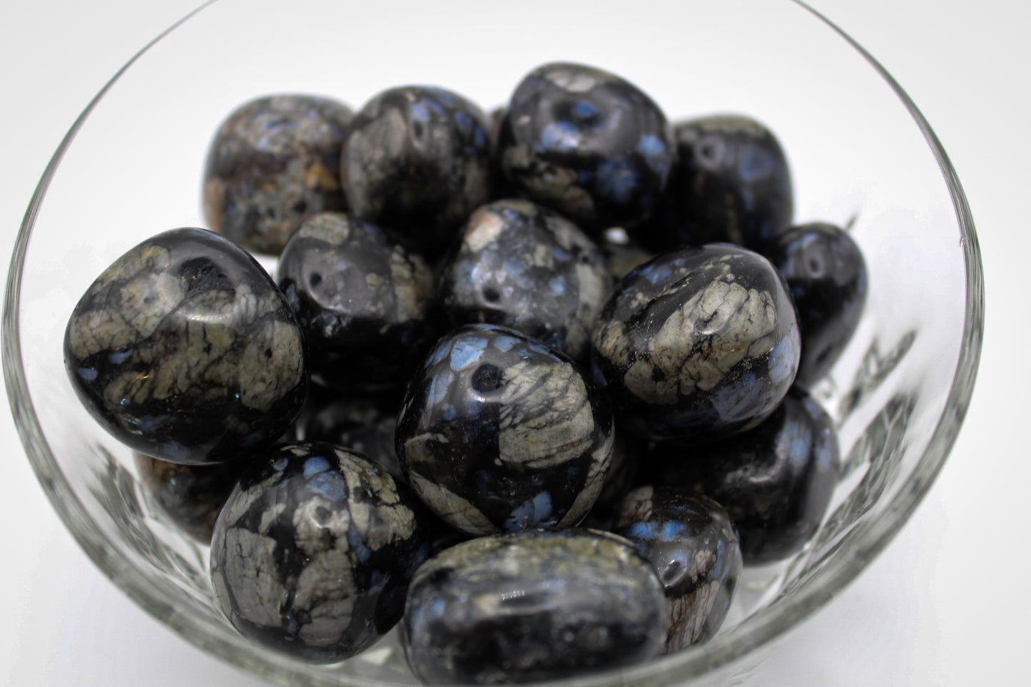 A collection of polished glaucophane stones displayed in a clear glass bowl.