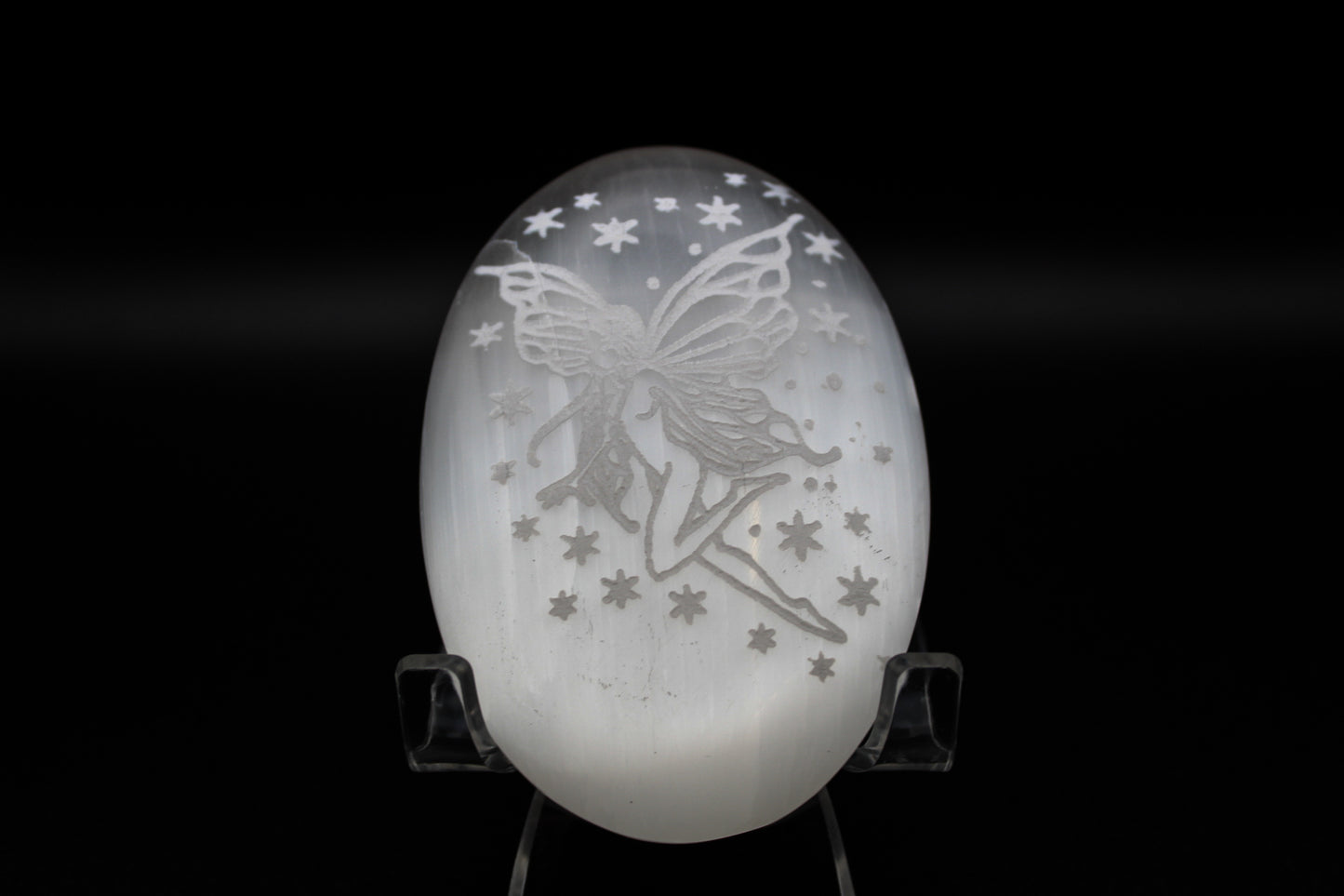 A white selenite fairy pillow with a silhouette of a fairy and stars etched on it.
