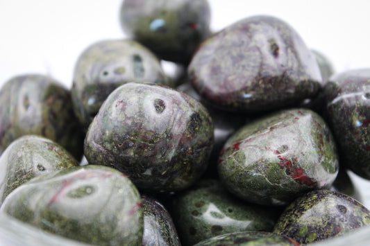 A collection of polished Dragon Bloodstone tumble stones displayed in a clear bowl.