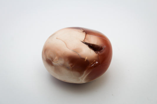 A polished carnelian stone with a smooth surface, showing natural variations in color from beige to brown.