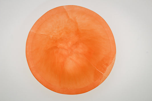 A round orange selenite crystal bowl on a white background.