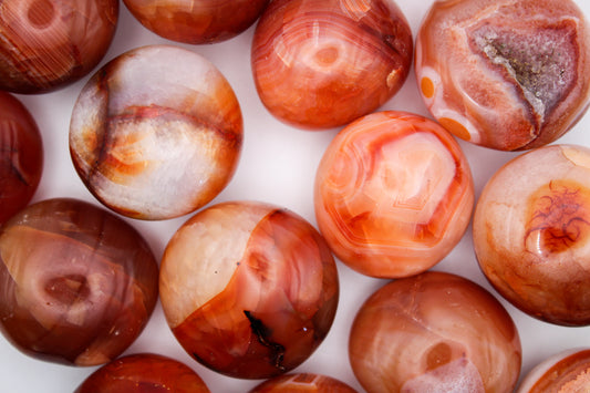 A collection of round carnelian stones with a smooth, polished finish, displaying a orange and white color palette.