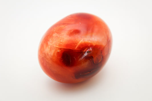 A polished carnelian stone with a high gloss finish, predominantly red in color with natural variations.