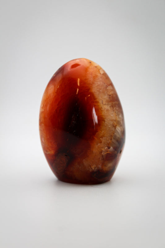 A polished carnelian stone with a free form shape, featuring an orange to red gradient color.