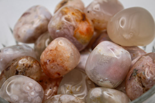 A collection of polished flower agate tumbles with varying shades of pink and white, contained in a clear glass bowl.