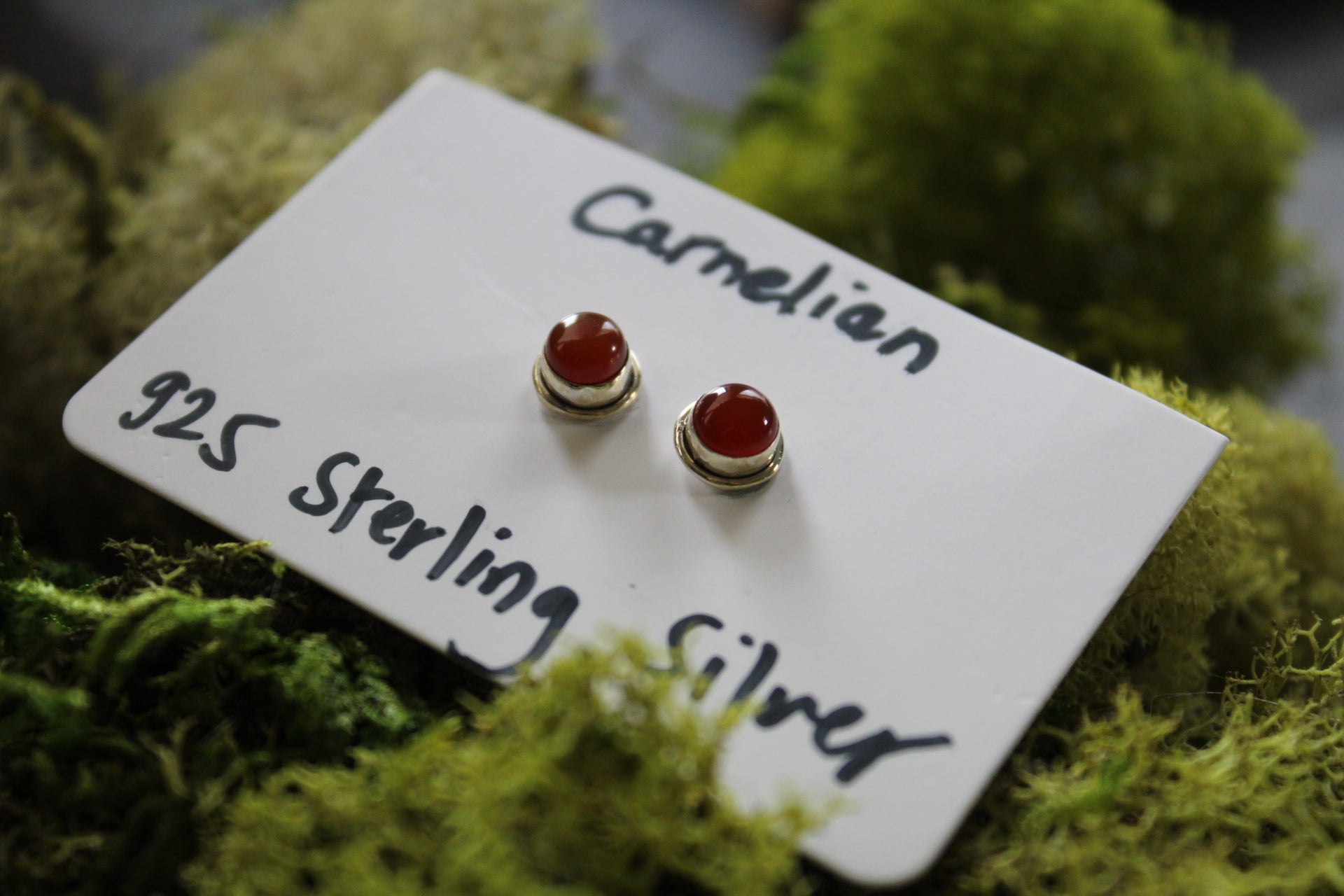 A pair of carnelian stone stud earrings with silver metallic caps.