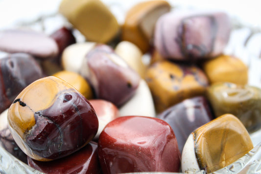 A collection of polished Mookaite tumbles in various colors placed in a clear glass dish.