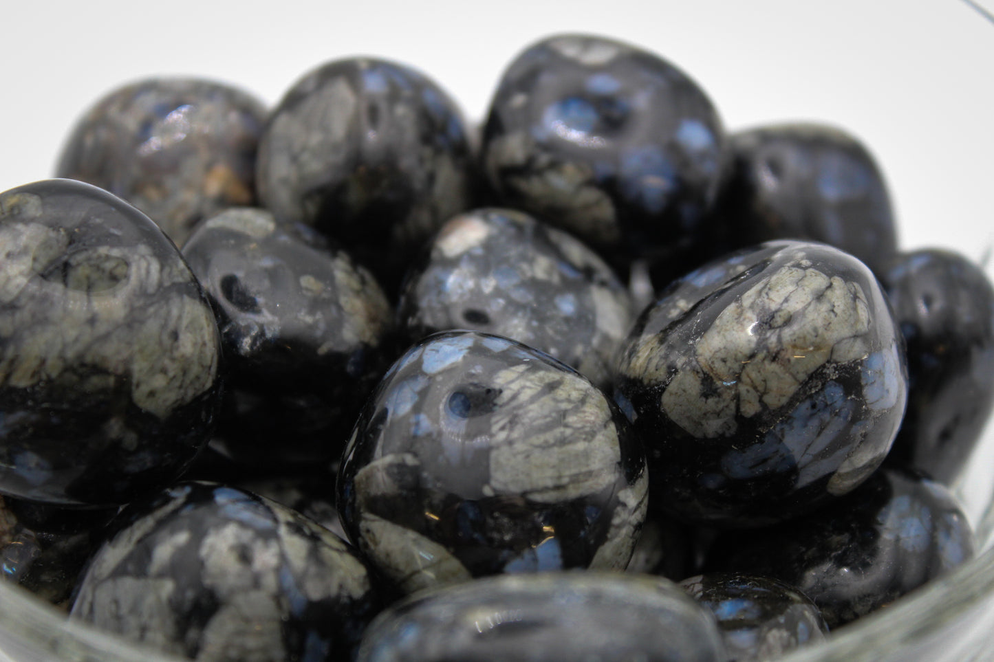 A collection of polished glaucophane stones displayed in a clear glass bowl.