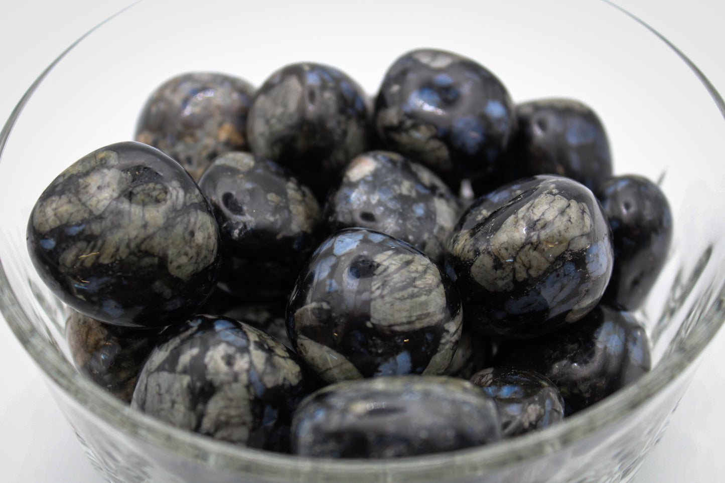A collection of polished glaucophane stones displayed in a clear glass bowl.