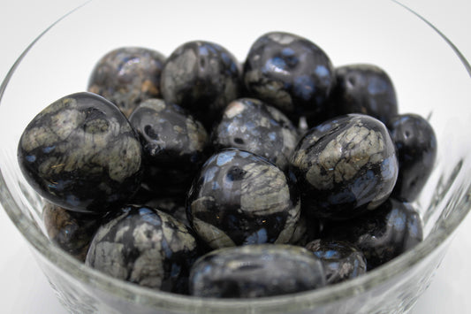 A collection of polished glaucophane stones displayed in a clear glass bowl.