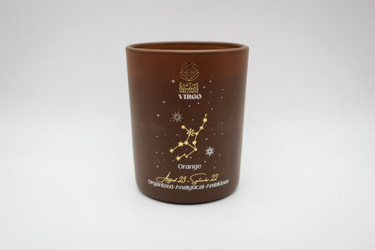 A brown candle with gold and white virgo constellation design.