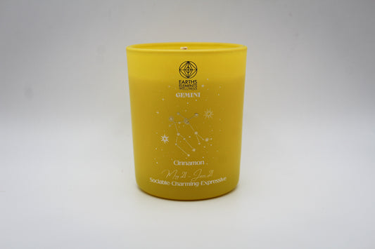 A yellow candle with white and silver geometric patterns and designs representing the constellation Gemini.