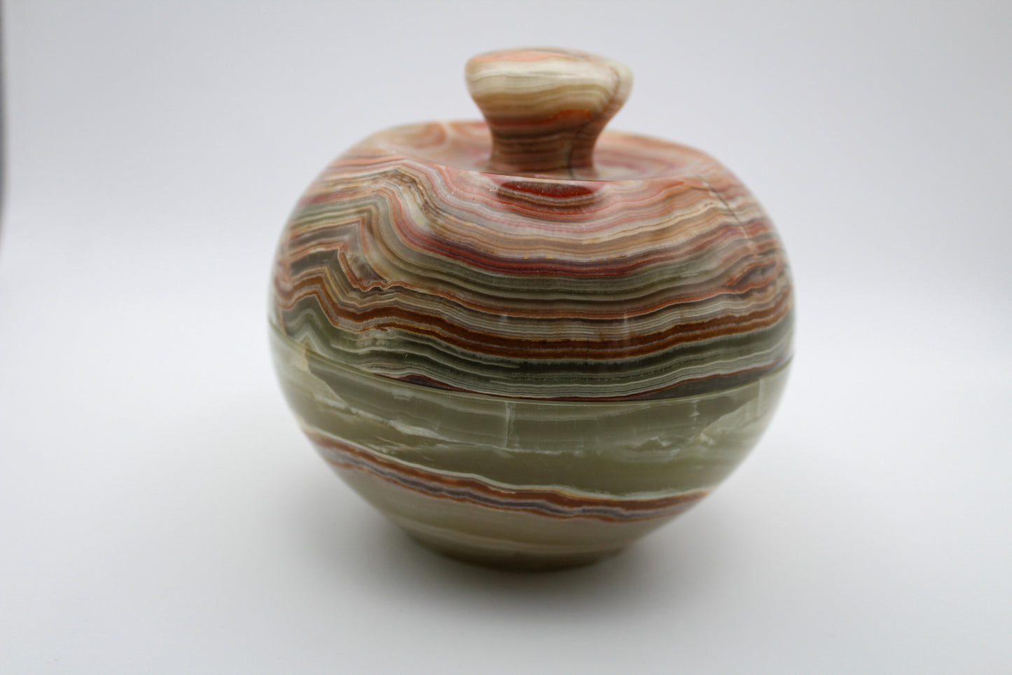 A polished onyx jar with a marbled red and white color pattern, resembling an apple, used for decoration.