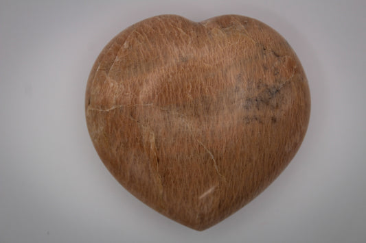 A polished heart-shaped peach moonstone with a smooth surface.