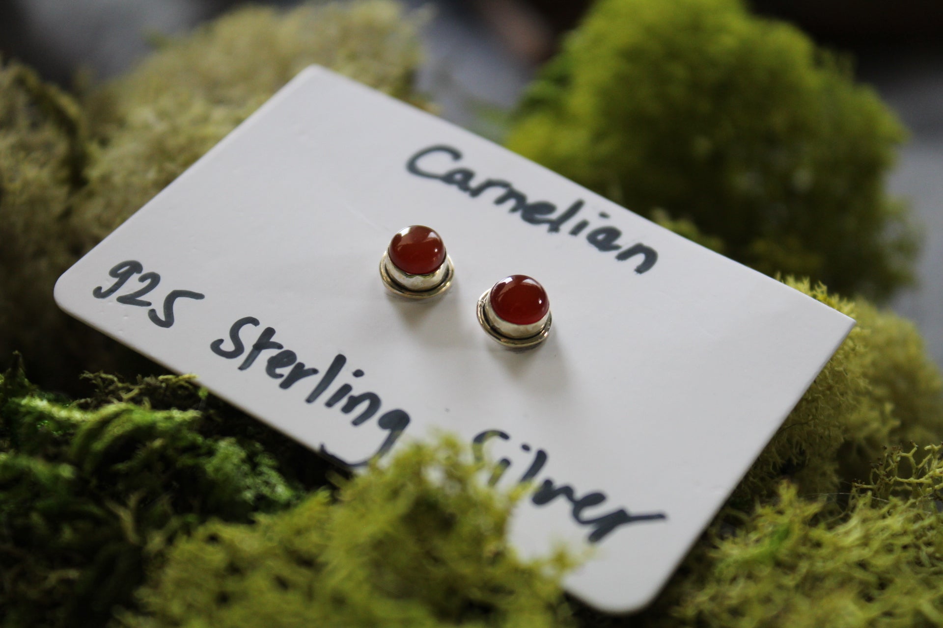 A pair of carnelian stone stud earrings with silver metallic caps.
