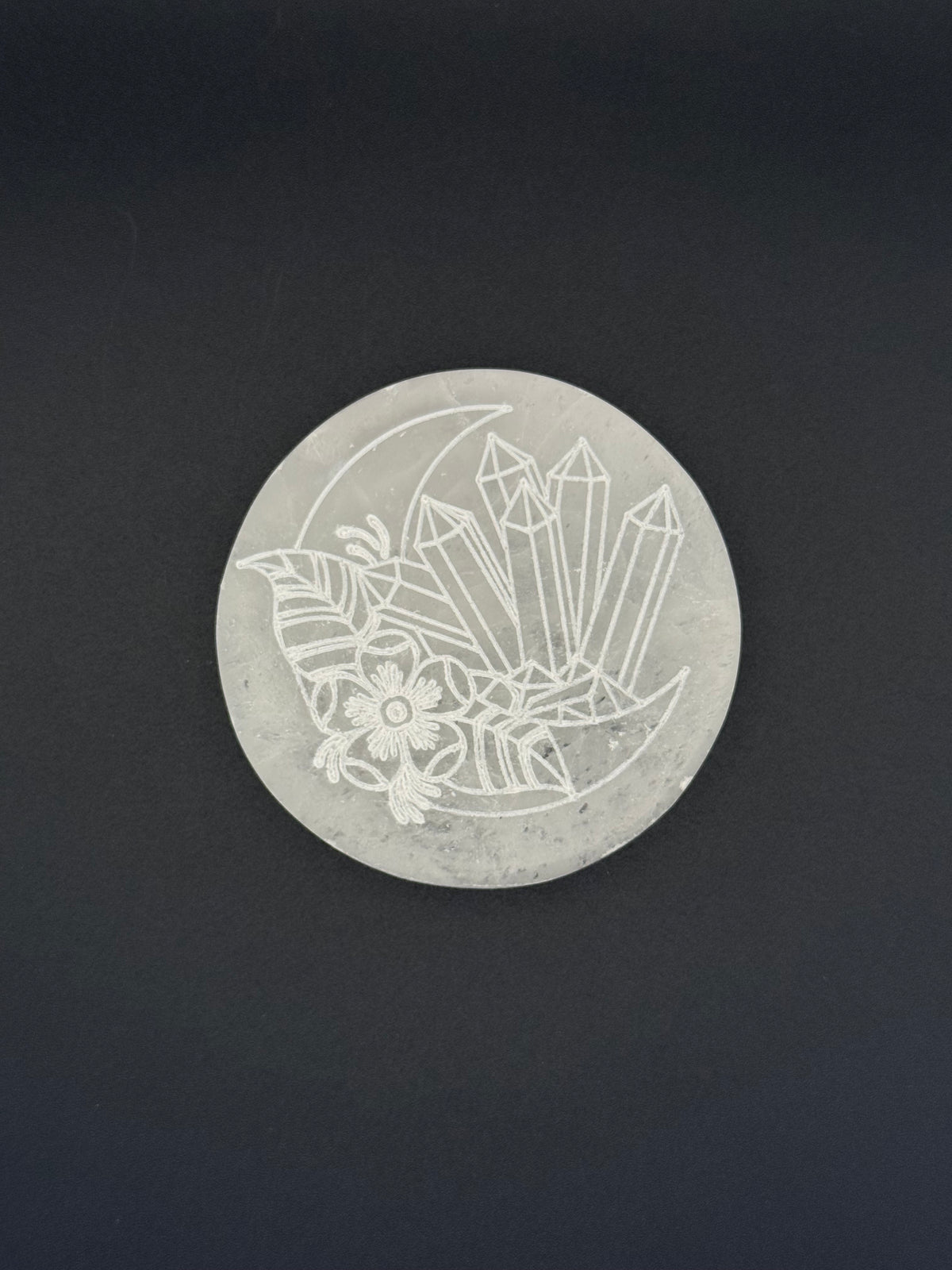 Selenite coaster with an engraved image of crystals and a moon.