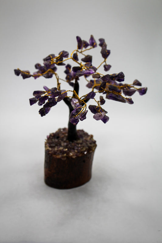 A sculpture of an amethyst crystal tree with gold-colored branches on a wooden base.