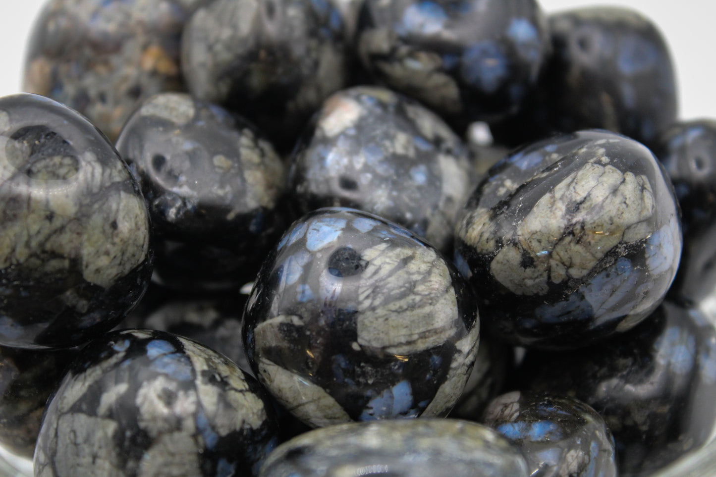A collection of polished glaucophane stones displayed in a clear glass bowl.