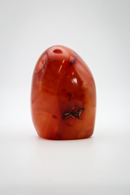 A polished carnelian stone with a free form shape, featuring an orange to red gradient color.