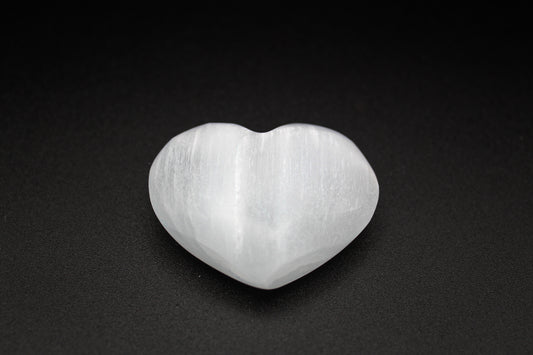 A heart-shaped selenite crystal on a dark background