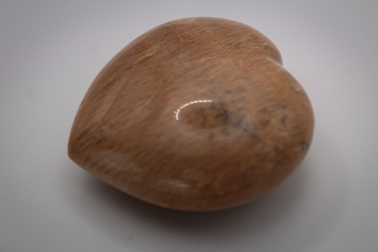 A polished heart-shaped peach moonstone with a smooth surface.