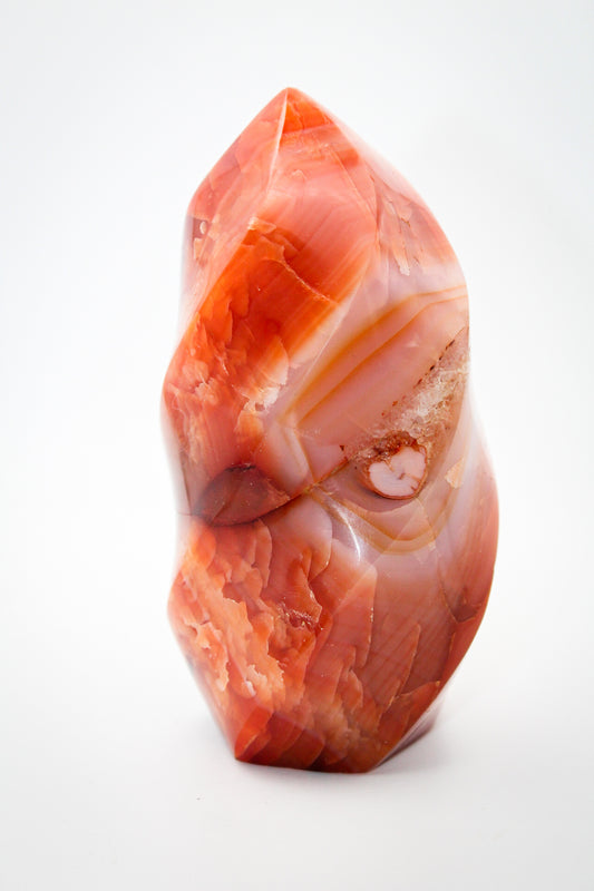 A polished carnelian stone in a flame shape with a red to orange gradient color.