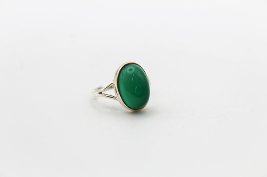 An oval green onyx ring set in a sterling silver band, displayed on a crystal.