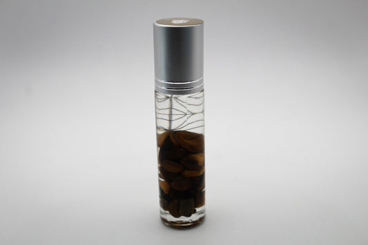 A clear glass roll-on bottle with a decorative design, containing essential oils and crystal chips.