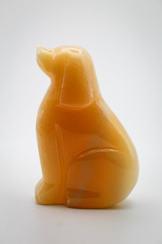 A polished calcite crystal carving in the shape of a dog, with an orange-yellow color.
