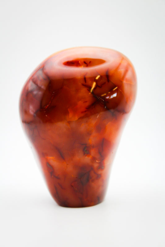 A polished carnelian stone in an irregular free-form shape with a smooth surface.