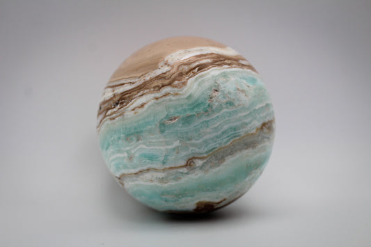 A polished Caribbean calcite sphere with bands of blue and brown colors.
