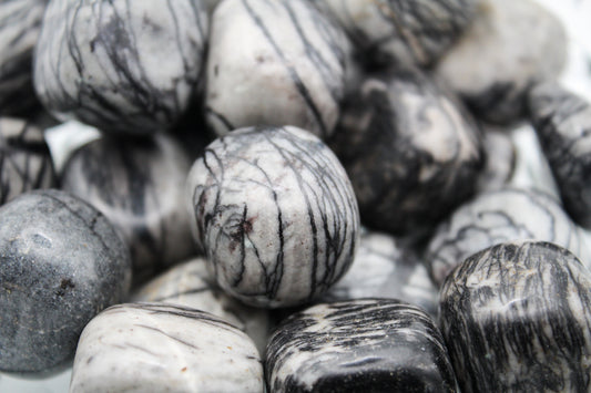 A collection of polished Zebra Jasper stones in various shades of black, gray, and white, arranged in a pile.
