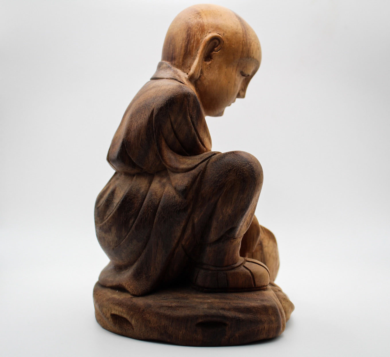 A wooden statue of a Buddha sitting and holding a fish.