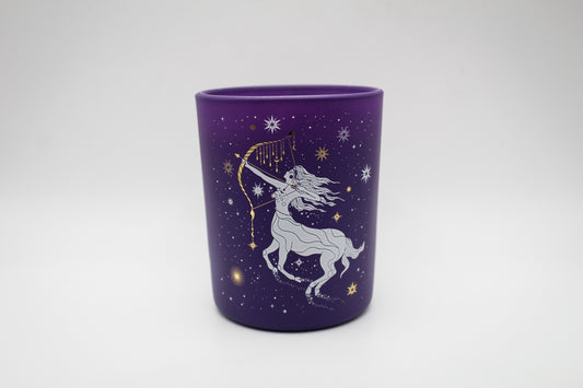 A purple candle with a Sagittarius sign design, featuring a centaur, stars, and a crescent moon.