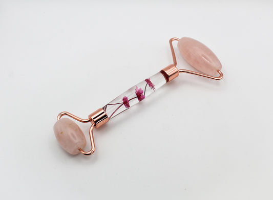 Massage roller with rose quartz rollers and pink flowers in the middle.