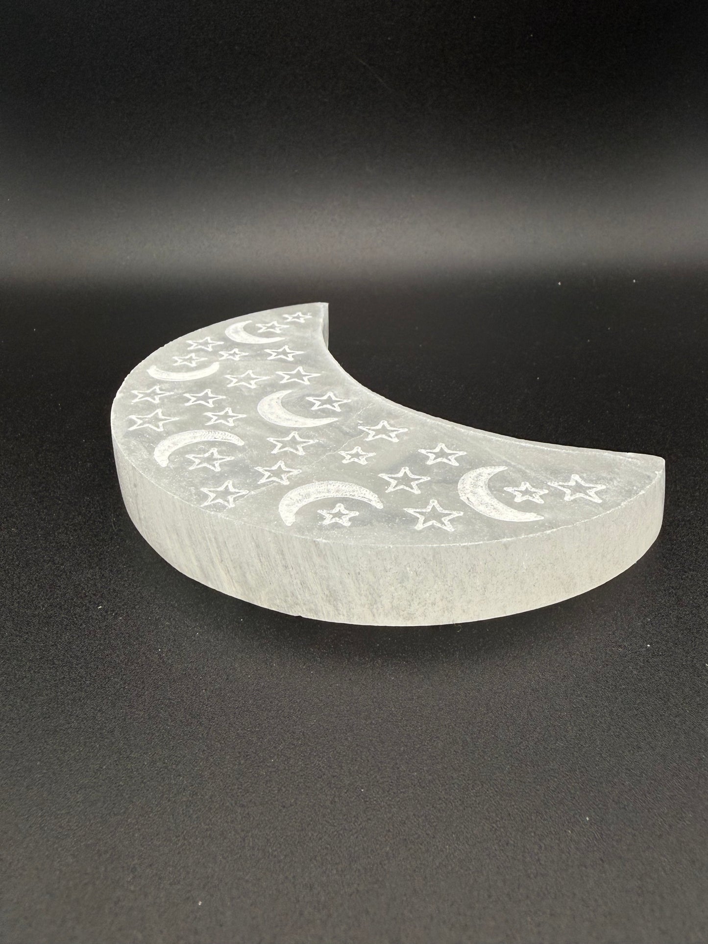Selenite in the shape of a moon with engraved moons and stars.