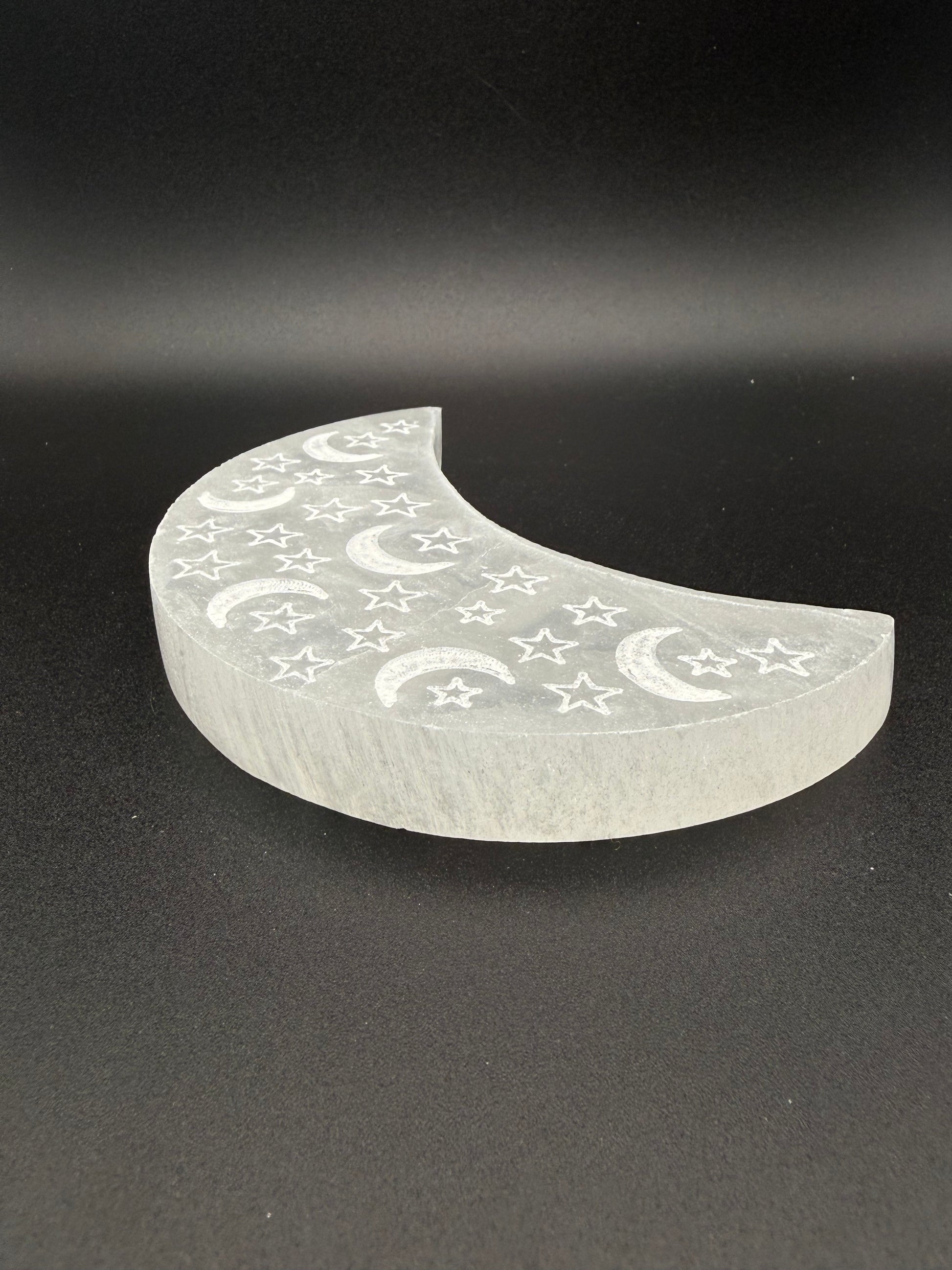 Selenite in the shape of a moon with engraved moons and stars.