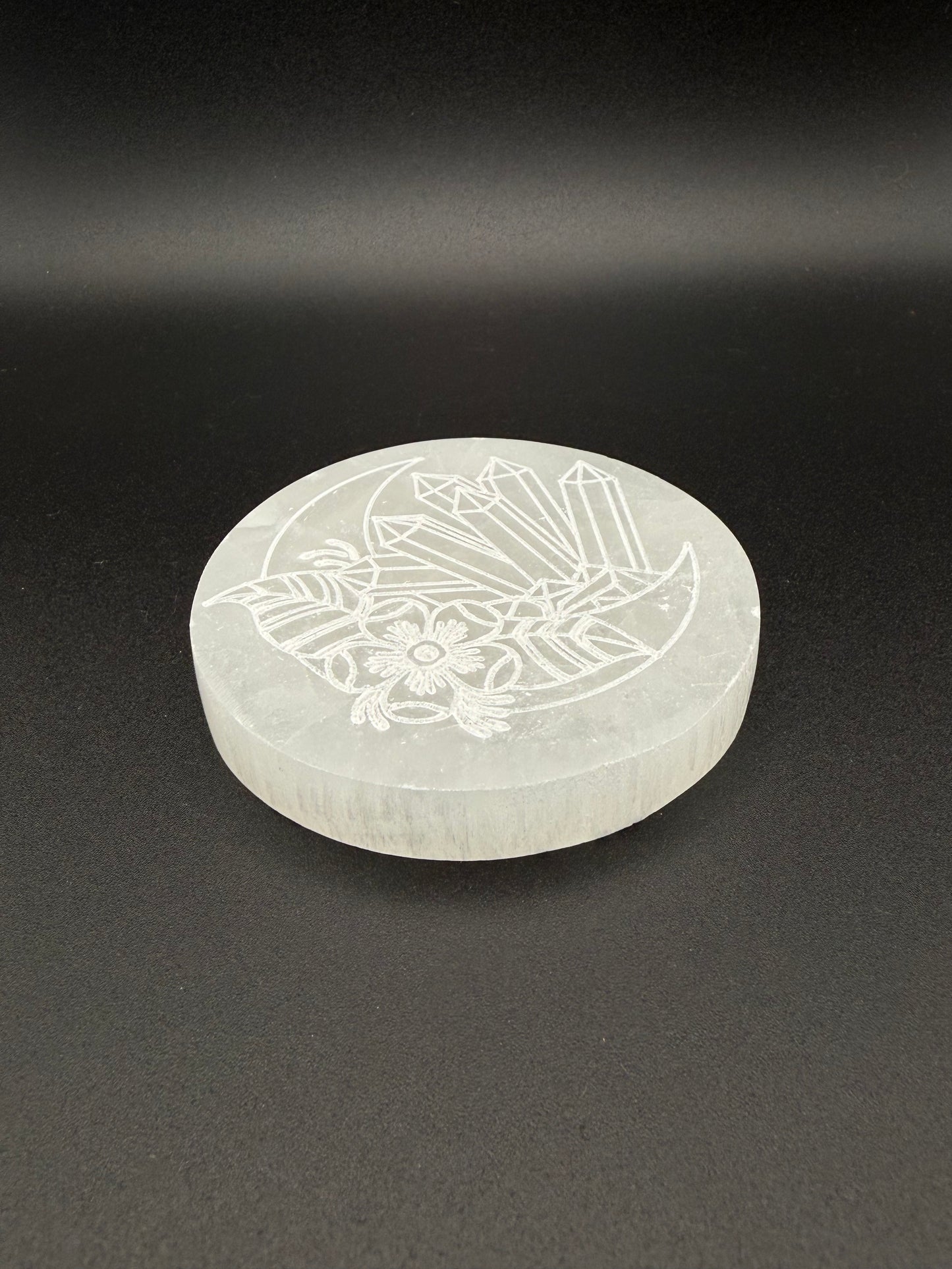 Selenite coaster with an engraved image of crystals and a moon.