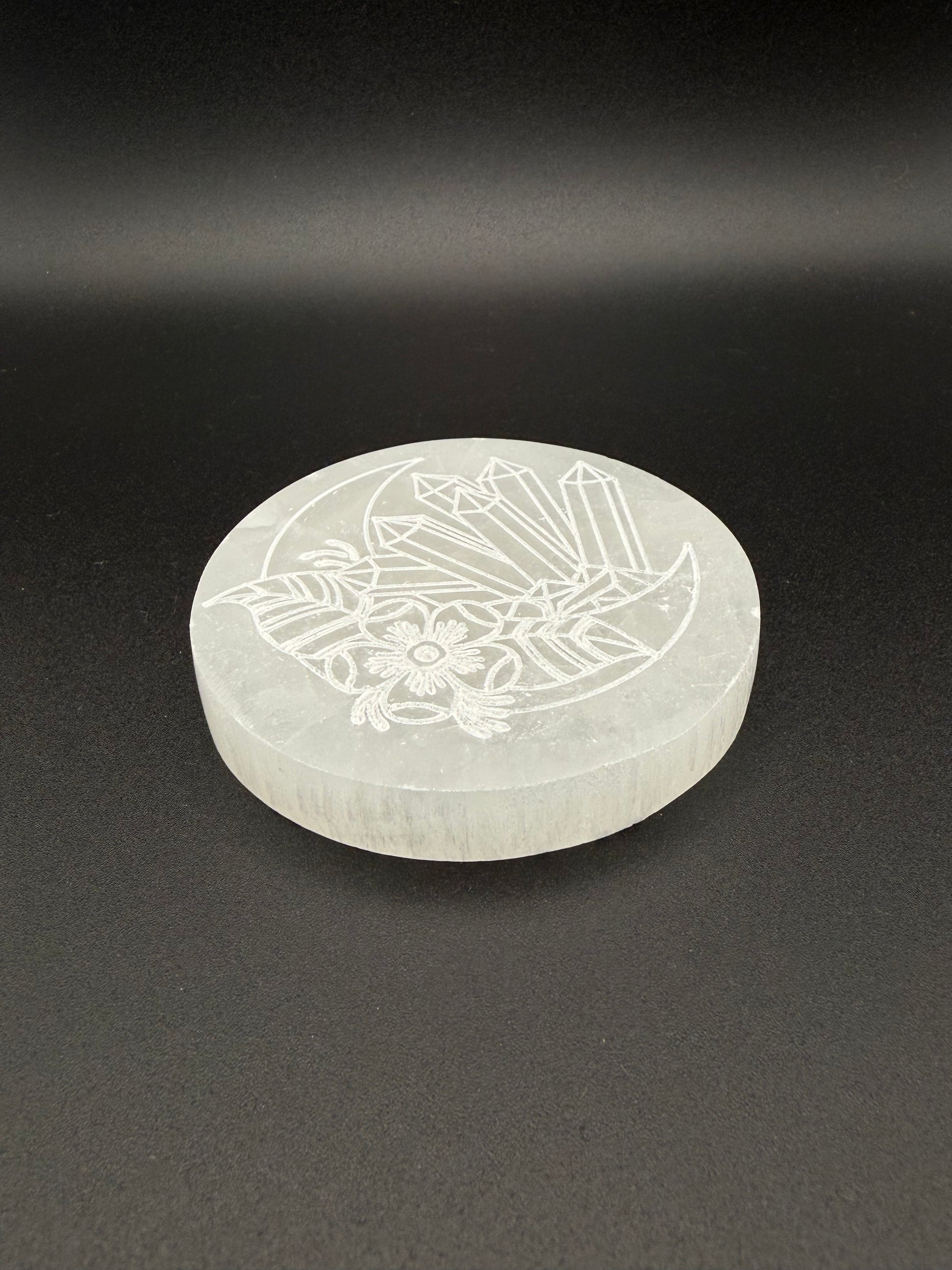 Selenite coaster with an engraved image of crystals and a moon.