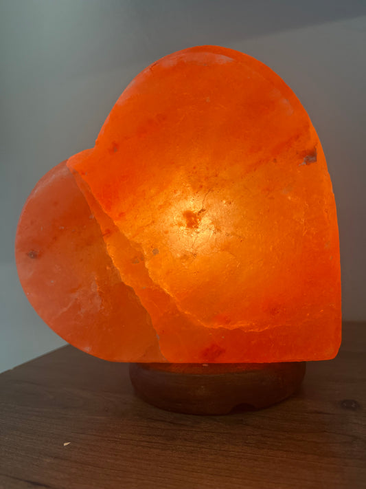 A heart-shaped Himalayan salt lamp glowing orange when illuminated.