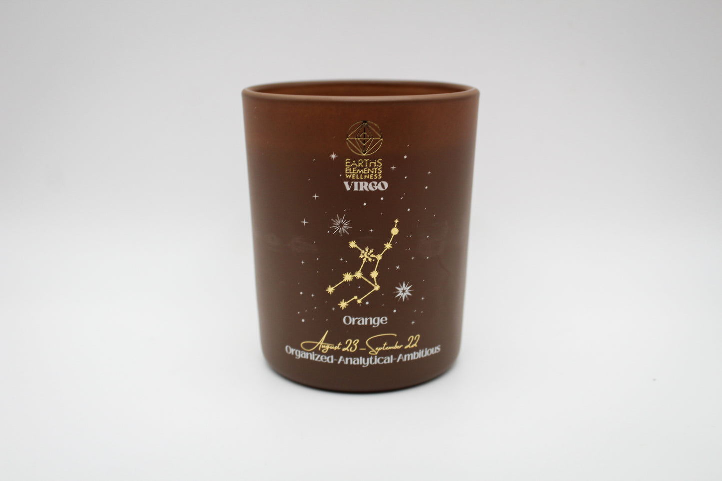 A brown candle with gold and white virgo constellation design.
