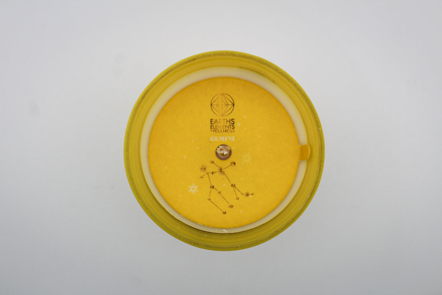 A yellow candle with white and silver geometric patterns and designs representing the constellation Gemini.