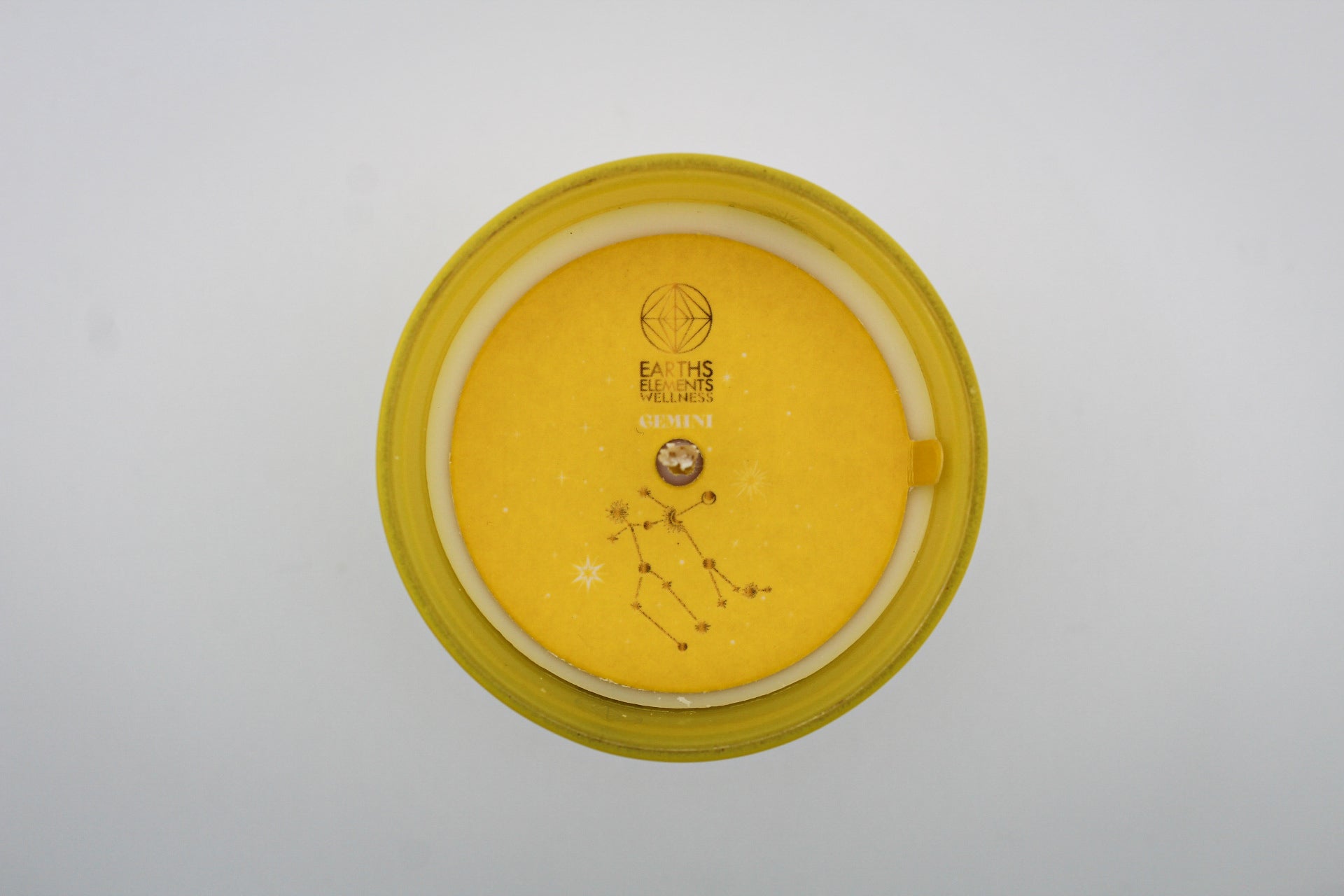 A yellow candle with white and silver geometric patterns and designs representing the constellation Gemini.