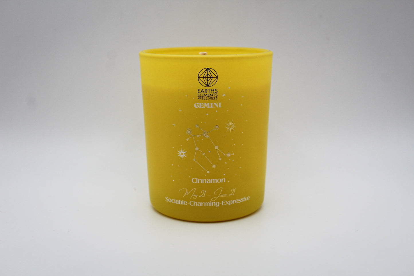 A yellow candle with white and silver geometric patterns and designs representing the constellation Gemini.