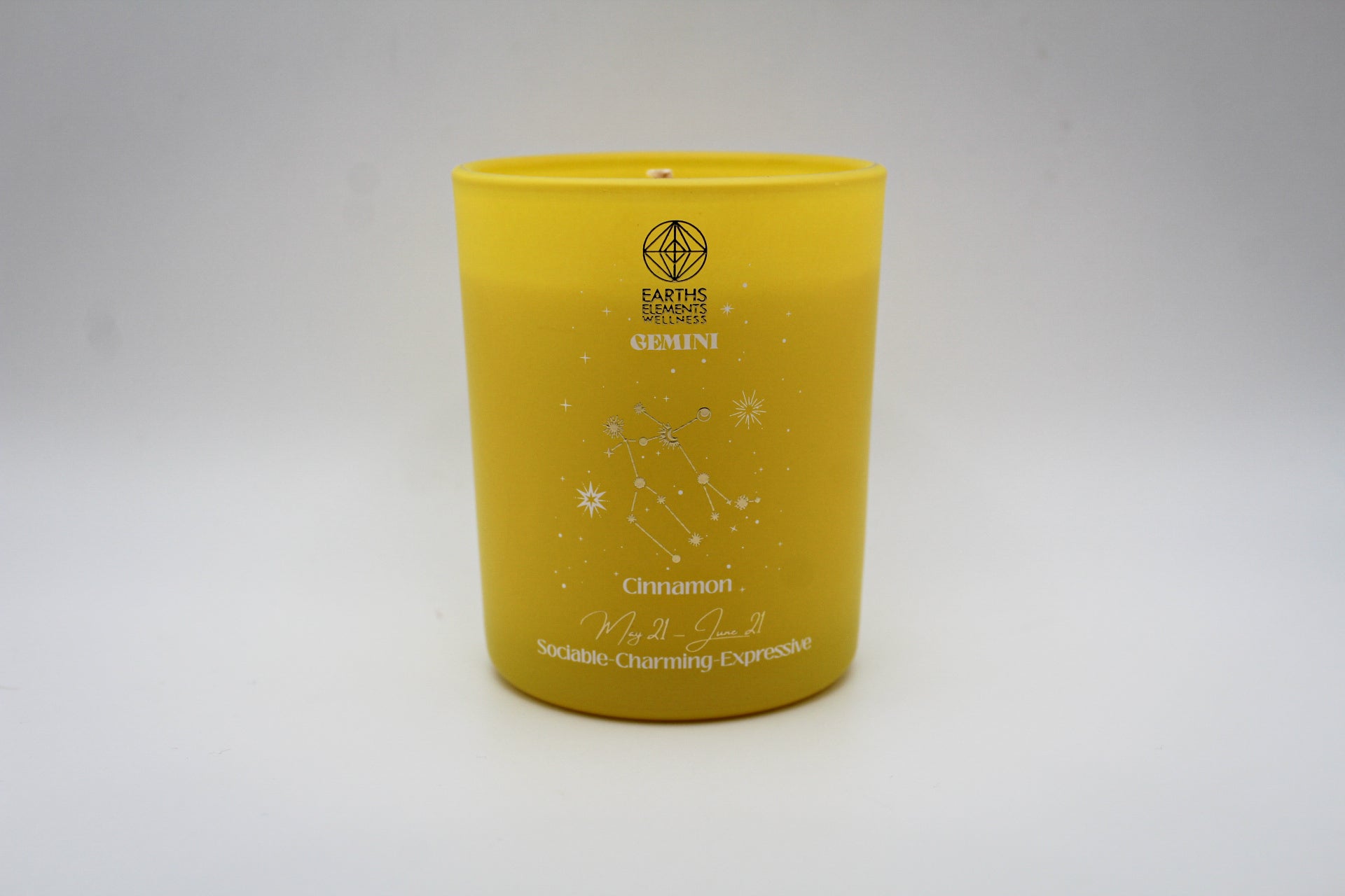 A yellow candle with white and silver geometric patterns and designs representing the constellation Gemini.