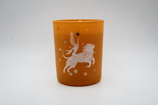 An orange candle with a white lion design and star patterns on it.