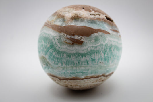 A polished Caribbean calcite sphere with bands of blue and brown colors.