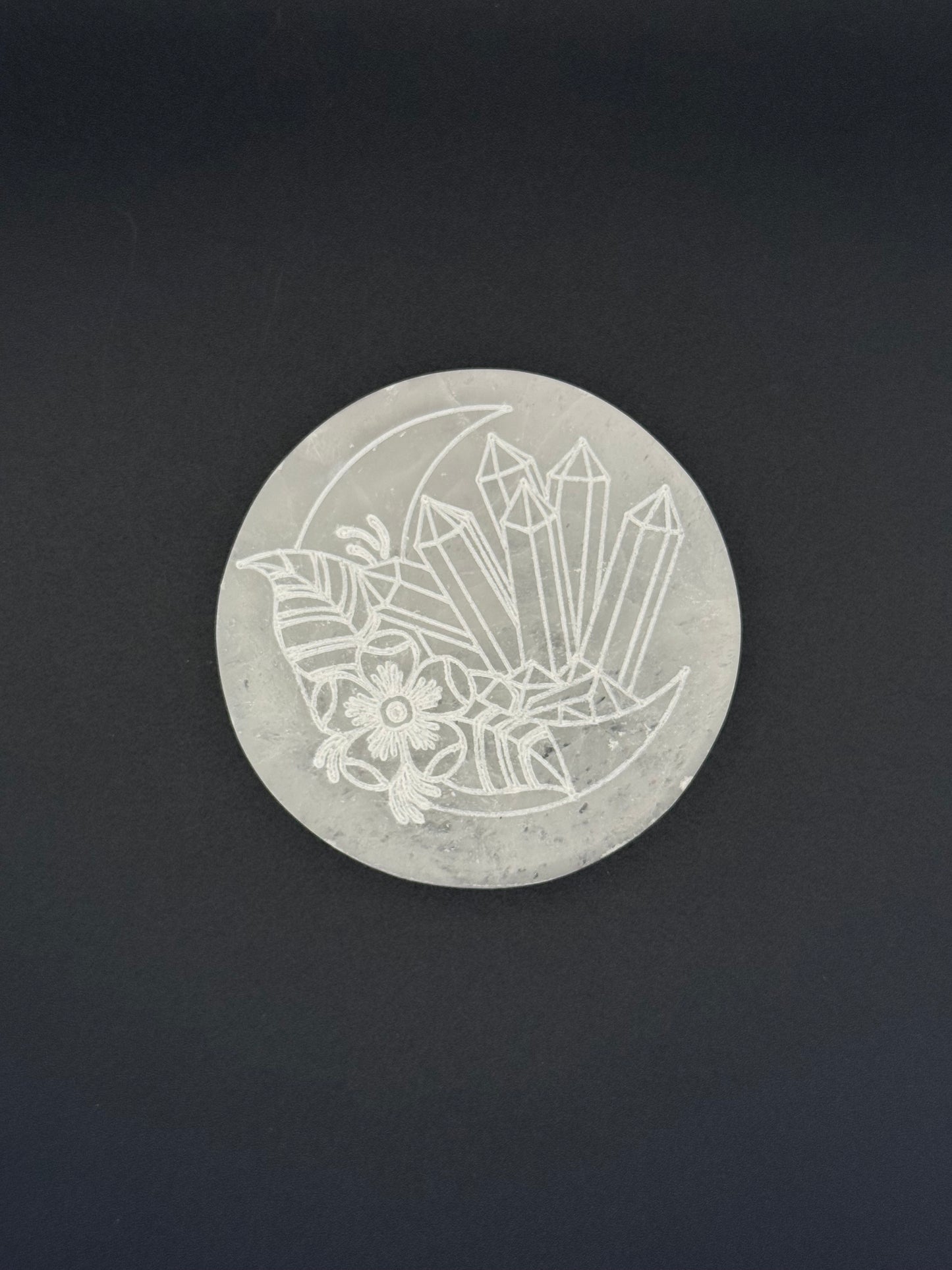 Selenite coaster with an engraved image of crystals and a moon.