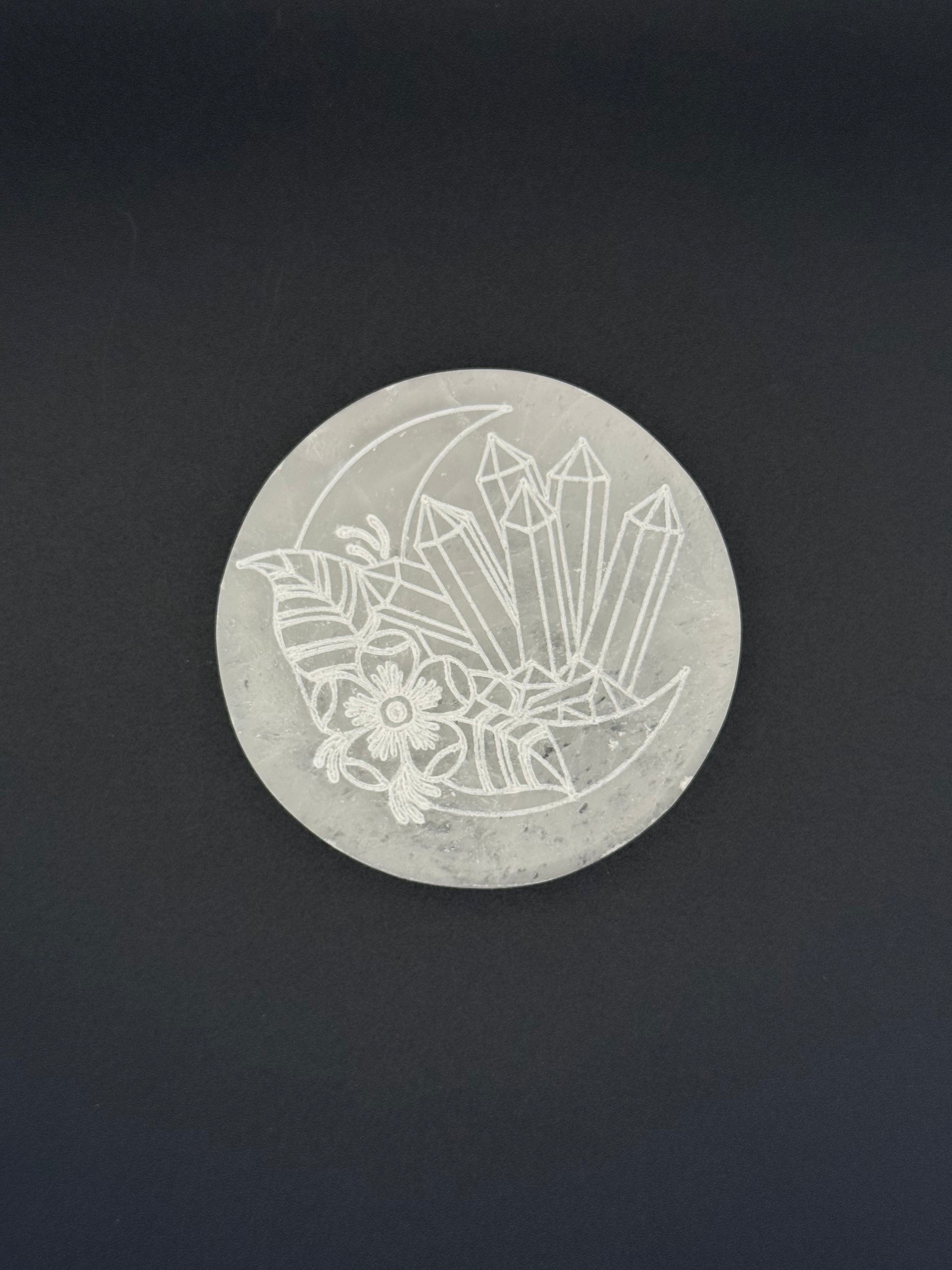 Selenite coaster with an engraved image of crystals and a moon.