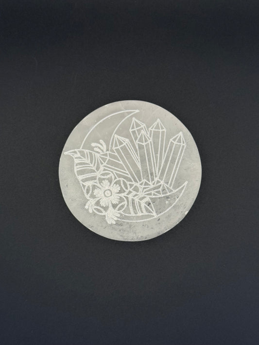 Selenite coaster with an engraved image of crystals and a moon.